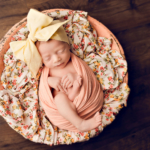 Beautiful Newborn baby girl posed in a bowl wearing a yellow bow by newborn photographer in Norfolk