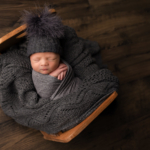 Beautiful Newborn baby boy posed in a wooden crib by newborn photographer in Norfolk