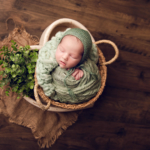 Beautiful Newborn baby boy posed in a basket wrapped in green by newborn photographer in Norfolk