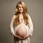 pregnant woman cradling her pregnant bump wearing a white lace gown by maternity photographer norfolk